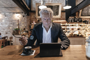 Älterer Geschäftsmann sitzt in einem Café, benutzt ein digitales Tablet und liest - GUSF00183