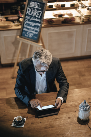 Älterer Geschäftsmann, der in einem Café sitzt und ein digitales Tablet benutzt, lizenzfreies Stockfoto