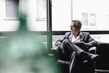 Senior businessman sitting in chair, reading newspaper - GUSF00188