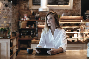 Blond woman sitting in cafe, using tablet, thinking - GUSF00200