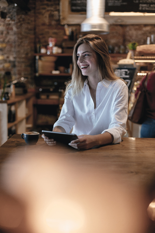 Lachende blonde Frau, die in einem Café sitzt und ein Tablet benutzt, lizenzfreies Stockfoto
