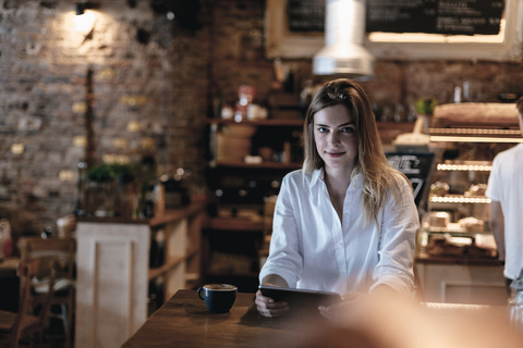 Lächelnde blonde Frau, die in einem Café sitzt und ein Tablet benutzt, lizenzfreies Stockfoto