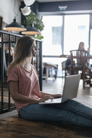 Junge Frau sitzt in einem Café und benutzt einen Laptop, lizenzfreies Stockfoto