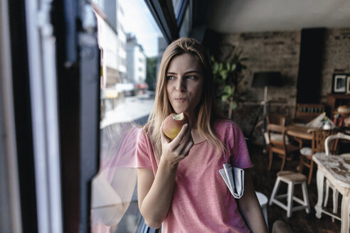 Junge Frau lehnt am Fenster und isst einen Apfel - GUSF00212