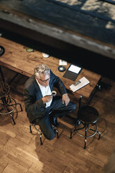 Älterer Geschäftsmann sitzt in einem Café und trinkt Kaffee - GUSF00226
