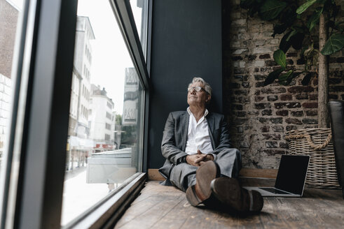 Businessman sitting on floor next to window, taking a break - GUSF00243