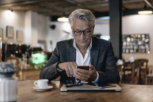 Älterer Geschäftsmann sitzt in einem Café und überprüft Nachrichten auf seinem Smartphone - GUSF00252