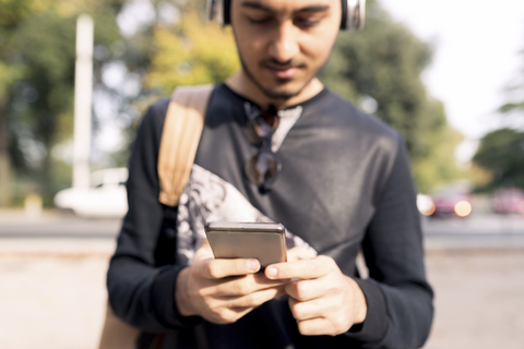 Junger Mann mit Kopfhörern und Mobiltelefon im Freien, lizenzfreies Stockfoto