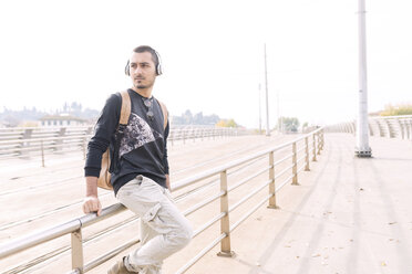 Young man with headphones and backpack at railing outdoors - FMOF00328