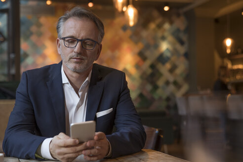 Porträt eines Geschäftsmannes, der in einem Restaurant sein Smartphone benutzt - SUF00347