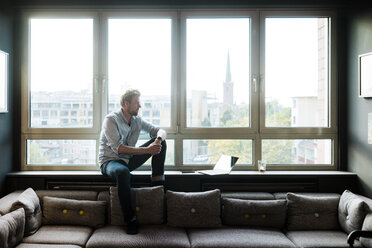 Geschäftsmann sitzt am Fenster im Aufenthaltsbereich eines Büros - JOSF02018