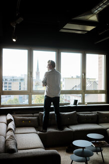 Geschäftsmann im Aufenthaltsraum eines Büros mit Blick aus dem Fenster - JOSF02020