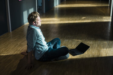 Geschäftsmann mit Laptop sitzt auf dem Boden im Büro - JOSF02022