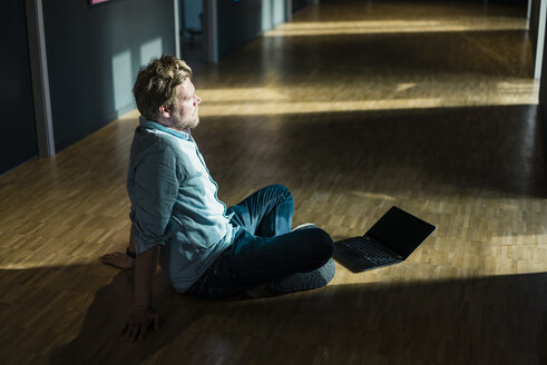 Geschäftsmann mit Laptop sitzt auf dem Boden im Büro - JOSF02022