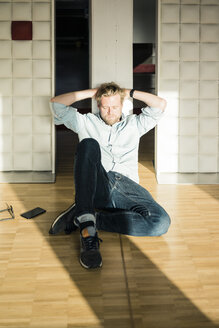 Entspannter Geschäftsmann im Büro, der auf dem Boden sitzt und sich gegen eine Wand lehnt - JOSF02024