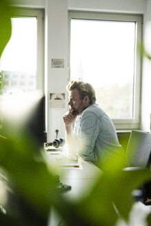 Geschäftsmann sitzt am Schreibtisch im Büro und denkt nach - JOSF02028