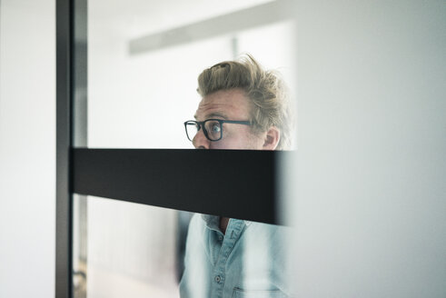 Geschäftsmann mit großen Augen hinter Glasscheibe im Büro - JOSF02039