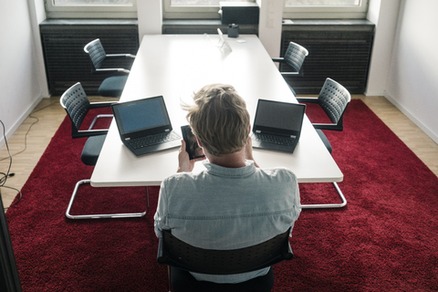 Geschäftsmann im Konferenzraum eines Büros mit zwei Laptops, lizenzfreies Stockfoto