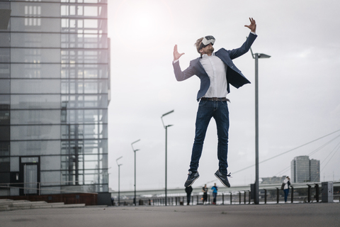 Geschäftsmann mit VR-Brille beim Springen in der Stadt, lizenzfreies Stockfoto