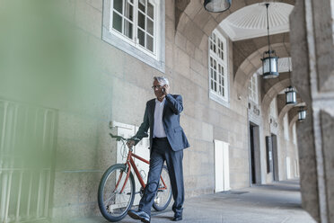 Älterer Geschäftsmann, der telefoniert und ein Fahrrad schiebt - GUSF00254