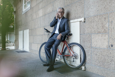 Senior businessman talking on the phone, leaning on bicycle - GUSF00255