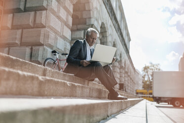 Älterer Geschäftsmann sitzt auf einer Treppe und benutzt einen Laptop - GUSF00258