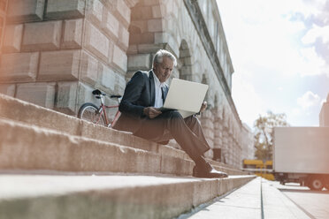 Senior businessman sitting on stairs, using laptop - GUSF00258