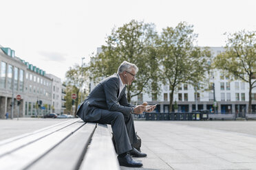ein älterer Geschäftsmann sitzt auf einer Treppe, telefoniert und isst Eiscreme - GUSF00259
