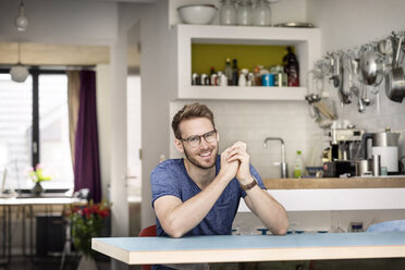 Porträt eines lächelnden jungen Mannes, der zu Hause am Küchentisch sitzt - PESF00751