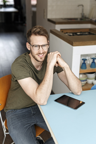 Portrait of smiling man with tablet in kitchen at home stock photo