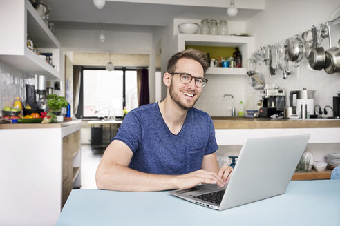 Portrait of smiling man using laptop in kitchen at home - PESF00759