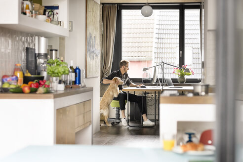 Mann mit Hund arbeitet am Schreibtisch zu Hause - PESF00760