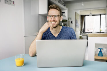 Portrait of smiling man using laptop in kitchen at home - PESF00761