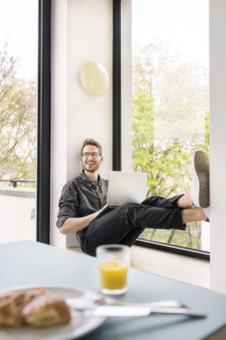 Happy man using laptop at the window at home stock photo