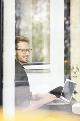 Porträt eines lächelnden Mannes mit Laptop am Fenster - PESF00769