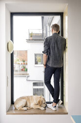 Man on the phone standing at the window next to dog - PESF00771