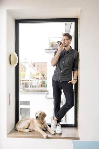 Man using smartphone at the window next to dog stock photo