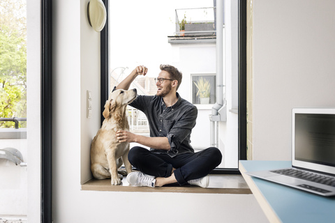 Glücklicher Mann mit Hund am Fenster sitzend, lizenzfreies Stockfoto