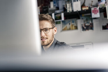 Porträt eines jungen Mannes hinter einem Computerbildschirm am Schreibtisch zu Hause - PESF00785