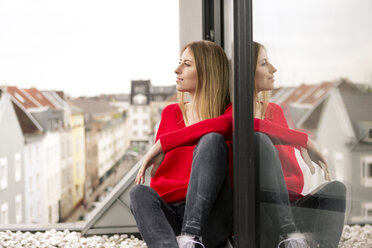 Lächelnde junge Frau sitzt am Fenster in einer Stadtwohnung - PESF00801
