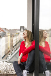 Lächelnde junge Frau sitzt am Fenster in einer Stadtwohnung - PESF00802