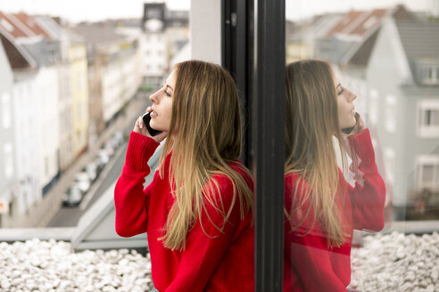 Junge Frau am Fenster in der Stadtwohnung am Handy - PESF00805