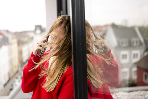 Lächelnde junge Frau am Fenster in der Stadtwohnung am Handy - PESF00806