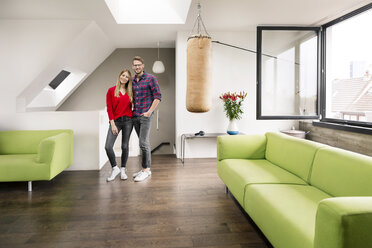 Porträt eines lächelnden jungen Paares, das zu Hause im Wohnzimmer steht - PESF00812