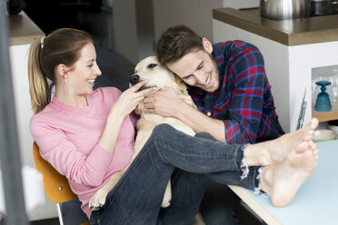 Happy young couple cuddling with dog at home - PESF00823