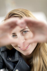 Portrait of smiling young woman shaping heart with her hands - PESF00825