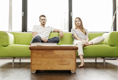 Porträt eines seriösen jungen Paares, das auf der Couch im heimischen Wohnzimmer sitzt - PESF00830
