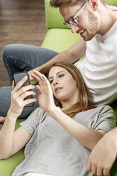 Young couple on couch in living room at home sharing cell phone - PESF00836