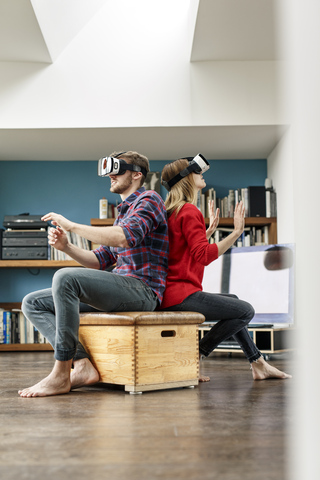 Young couple at home sitting on box wearing VR glasses stock photo