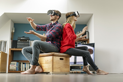 Young couple at home sitting on box wearing VR glasses stock photo